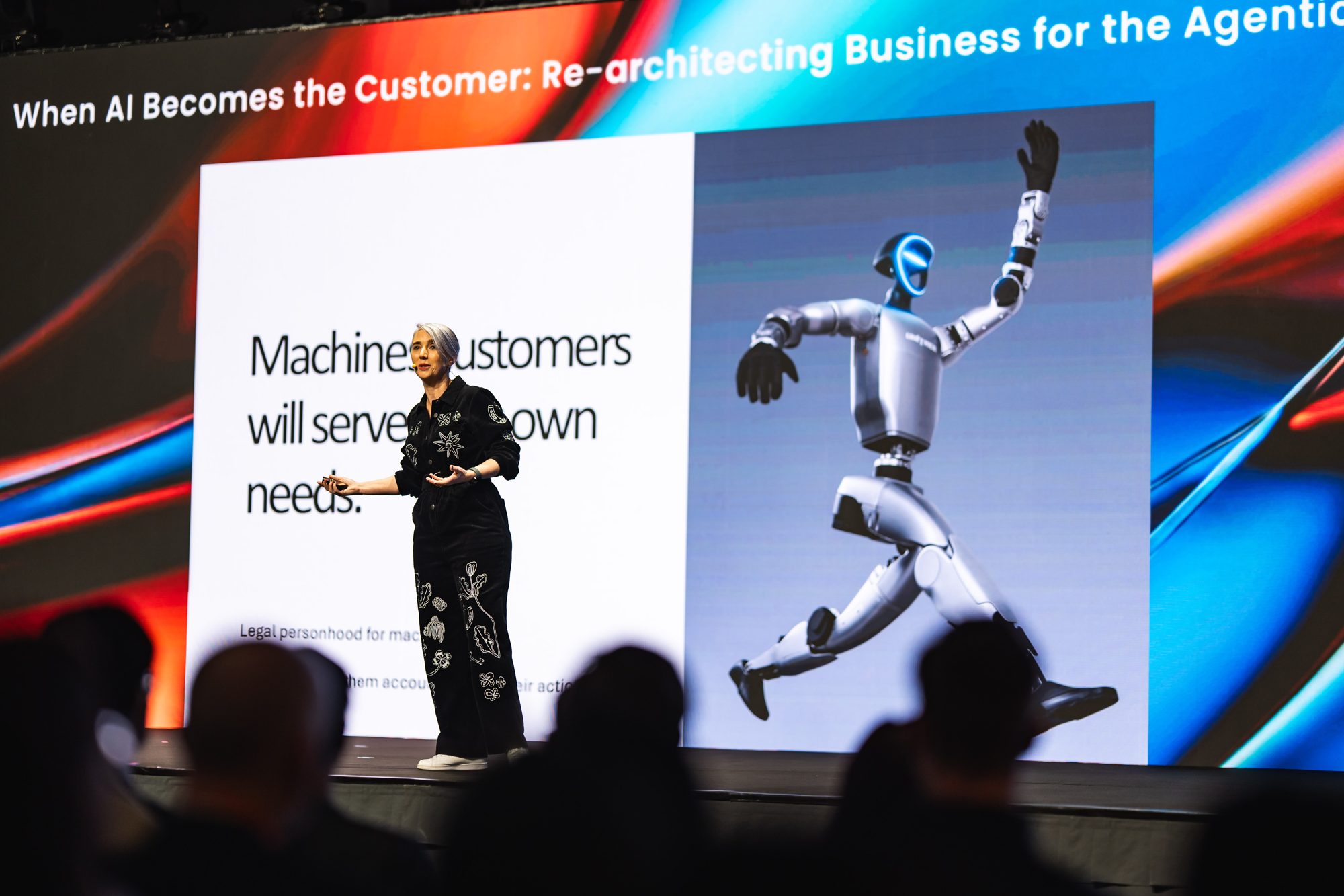 Katja Forbes on stage beside a slide with a leaping humanoid robot